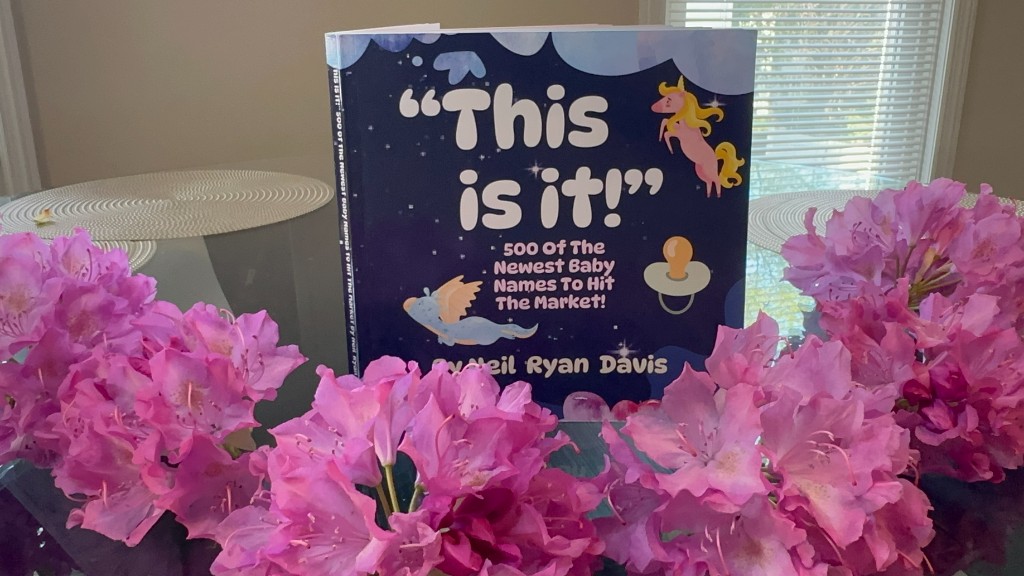 This is it! baby name book standing upright with pink flowers in the foreground